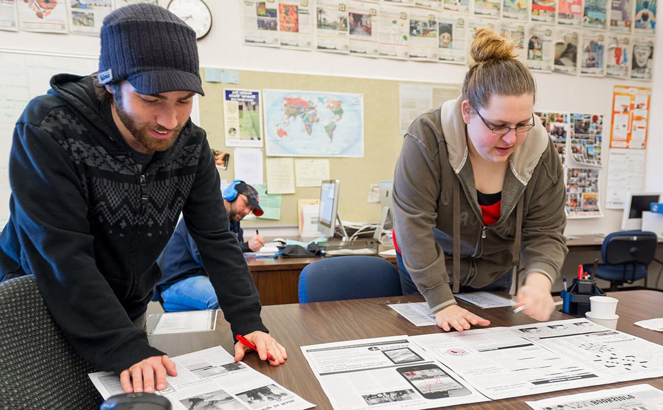 Female and male students working on newspaper layout in classroom